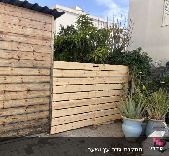 גדר עץ חדשה ליד עציצים וצמחייה בגינה